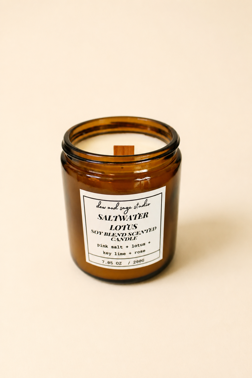 An amber glass jar candle with a white label reading 'SALTWATER' and 'LOTUS' by 'the wild orange studio', photographed on a warm cream background.