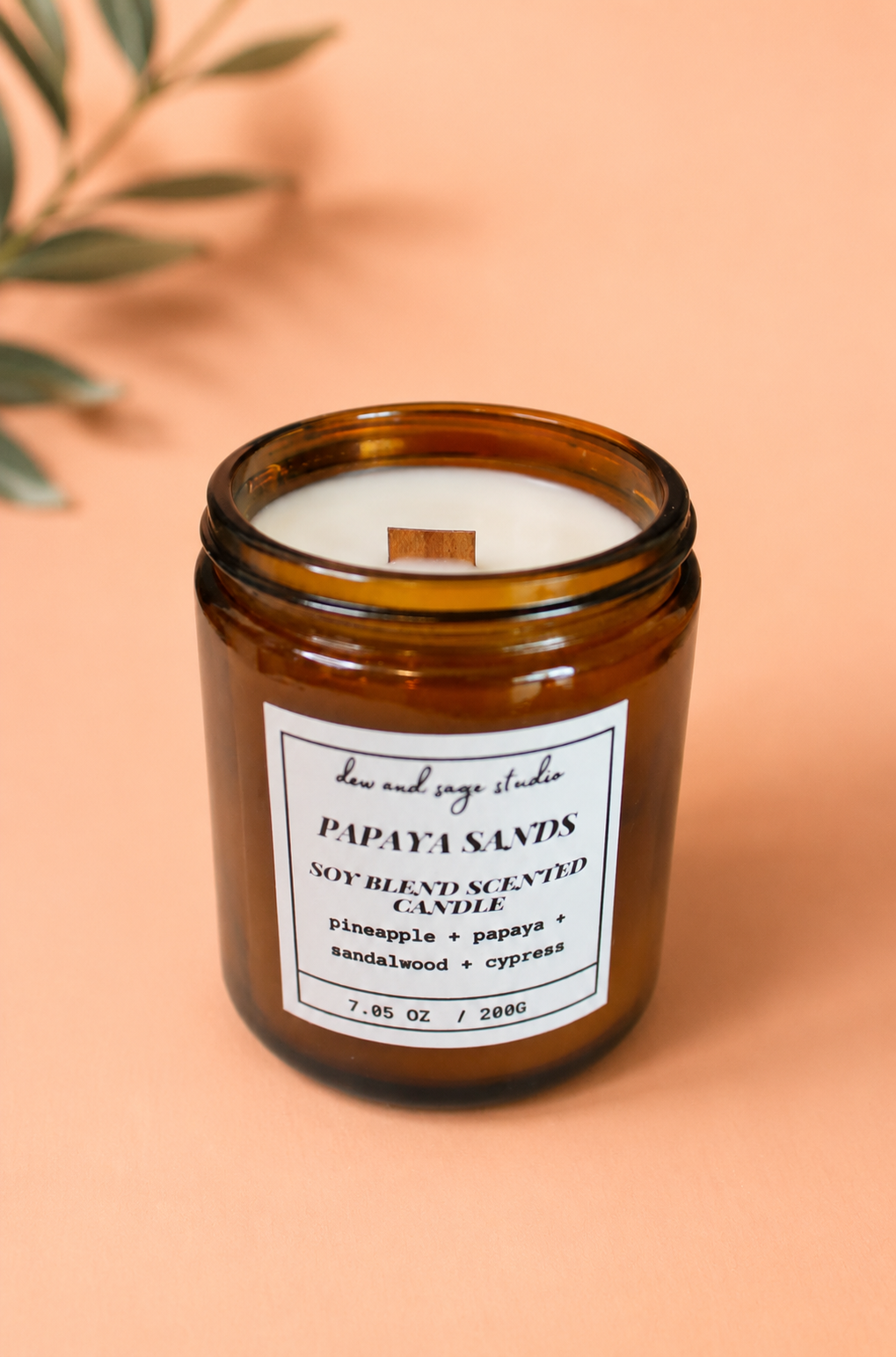 Candle in an amber jar with a label on a peach background