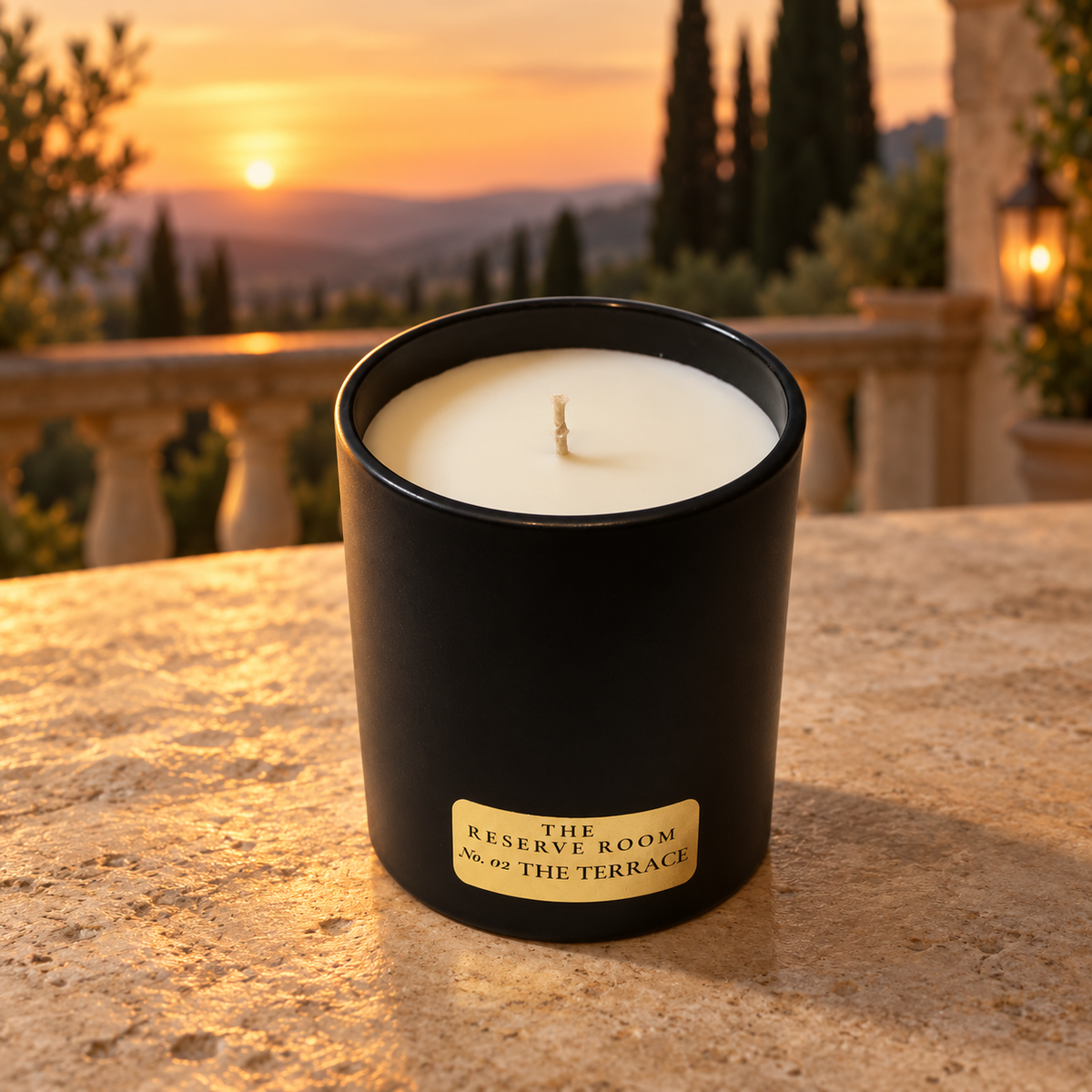 A black candle jar with a gold label reading 'THE RESERVE ROOM No. 07 THE TERRACE' sits on a stone terrace at sunset, with a blurred outdoor garden and railing in the background.