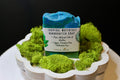 Handcrafted soap bar with a label on a bed of green moss in a decorative bowl.