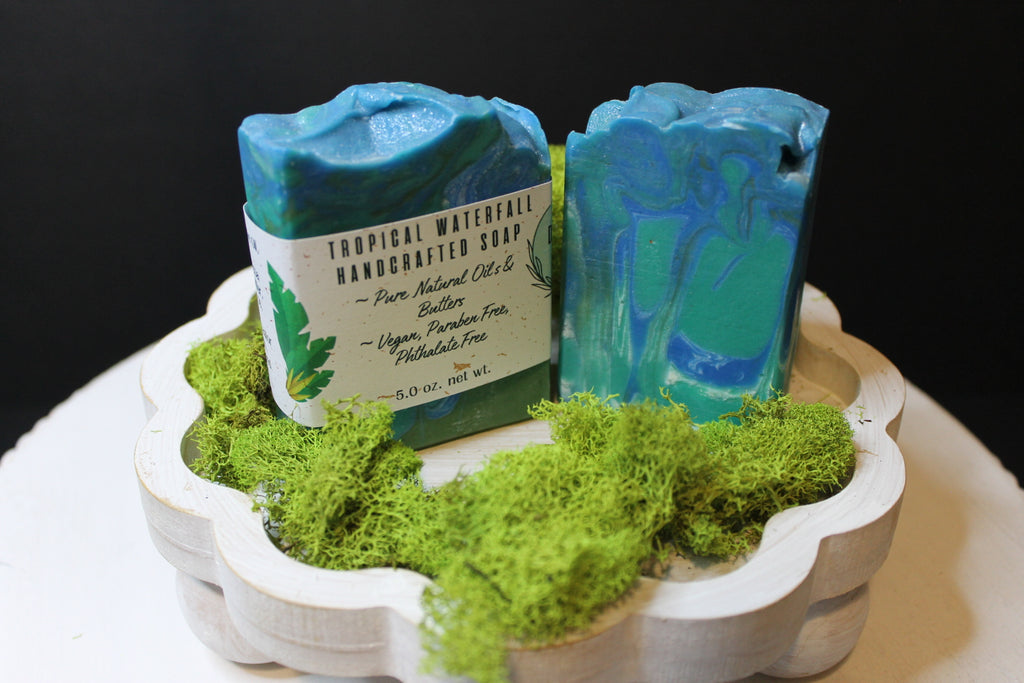 Two blue soaps on a decorative stand with greenery against a black background