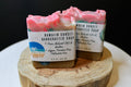 Two handcrafted soaps on a wooden block with visible labels.