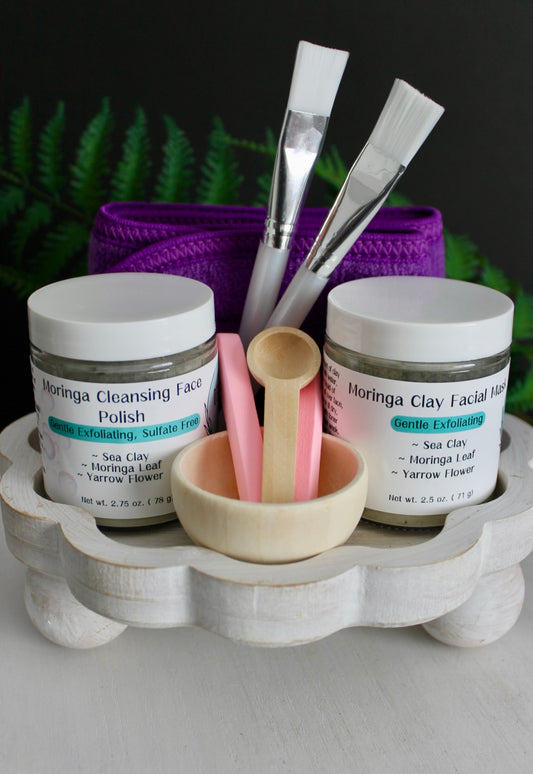 Cosmetic products including jars, brushes, and a bowl on a wooden stand with a dark background.