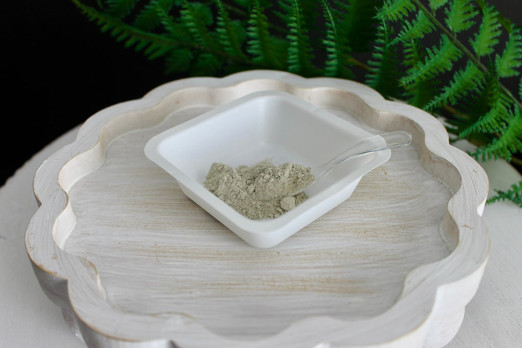 White ceramic dish with green powder on a decorative white plate against a dark background with greenery.
