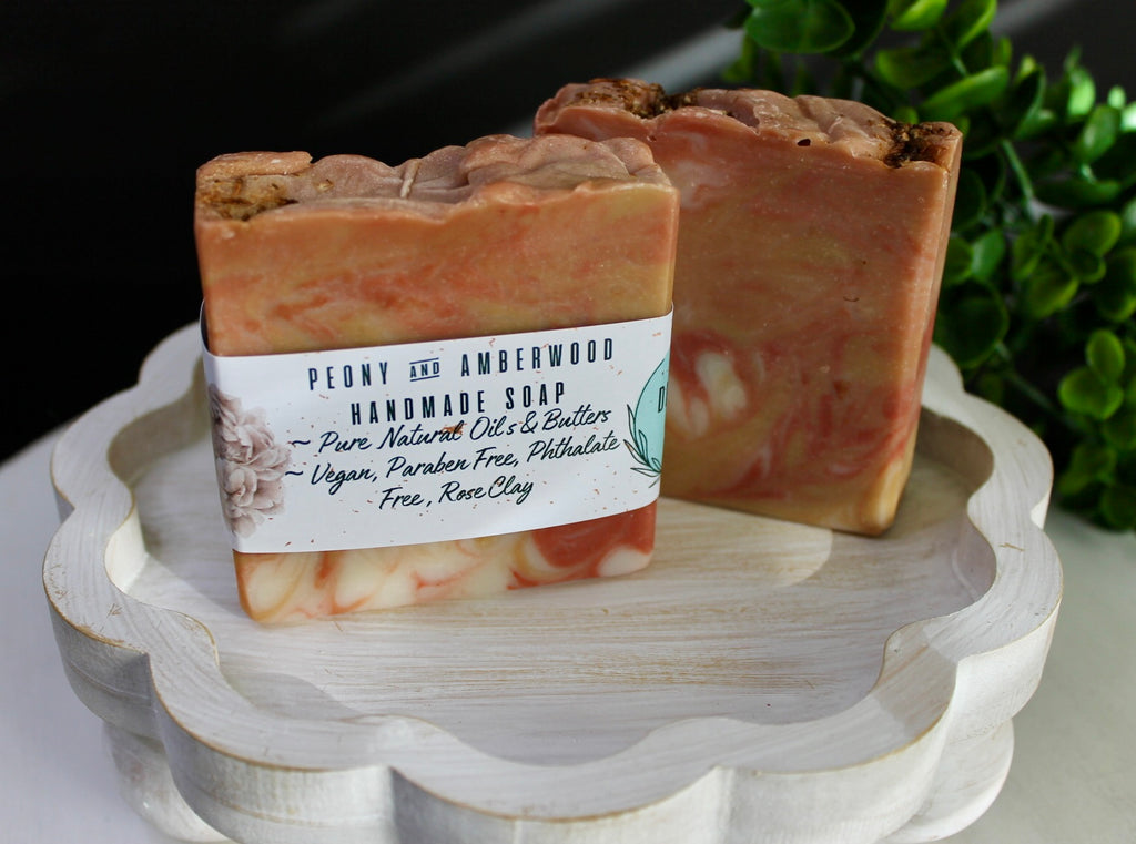 Two handmade soap bars on a decorative stand with a label in the foreground.