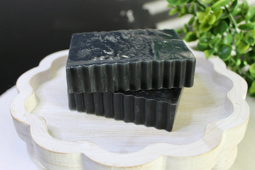 Two black soap bars on a decorative white stand with greenery in the background