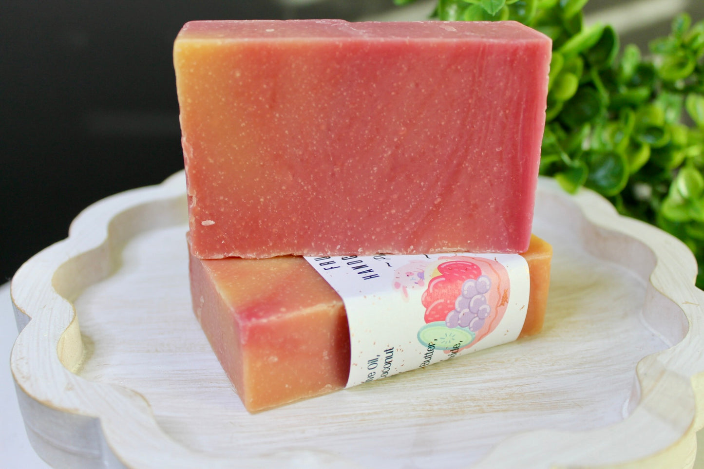 Two pink soap bars stacked on a white plate with a green leafy background
