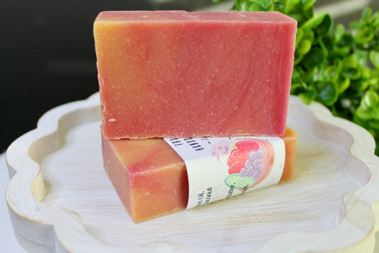 Two pink soap bars stacked on a white plate with a green leafy background