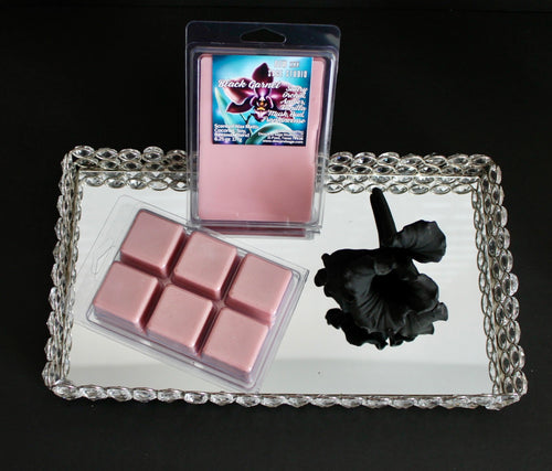 Pink wax melts in a clear packaging on a decorative tray with a black candle.