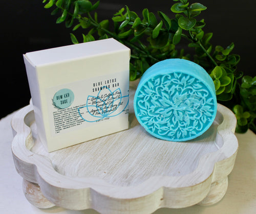 Bar of soap and blue decorative soap on a wooden stand with greenery in the background