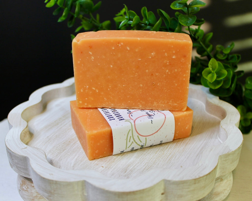 Two bars of orange soap on a decorative white stand with greenery in the background