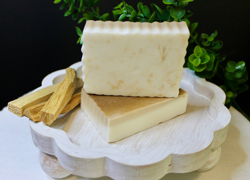 Two soap bars on a white stand with greenery in the background