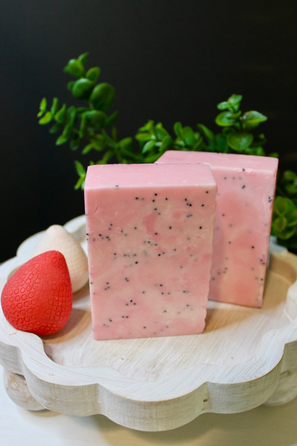 Pink soap bars with poppy seed specks on a white dish with a black background