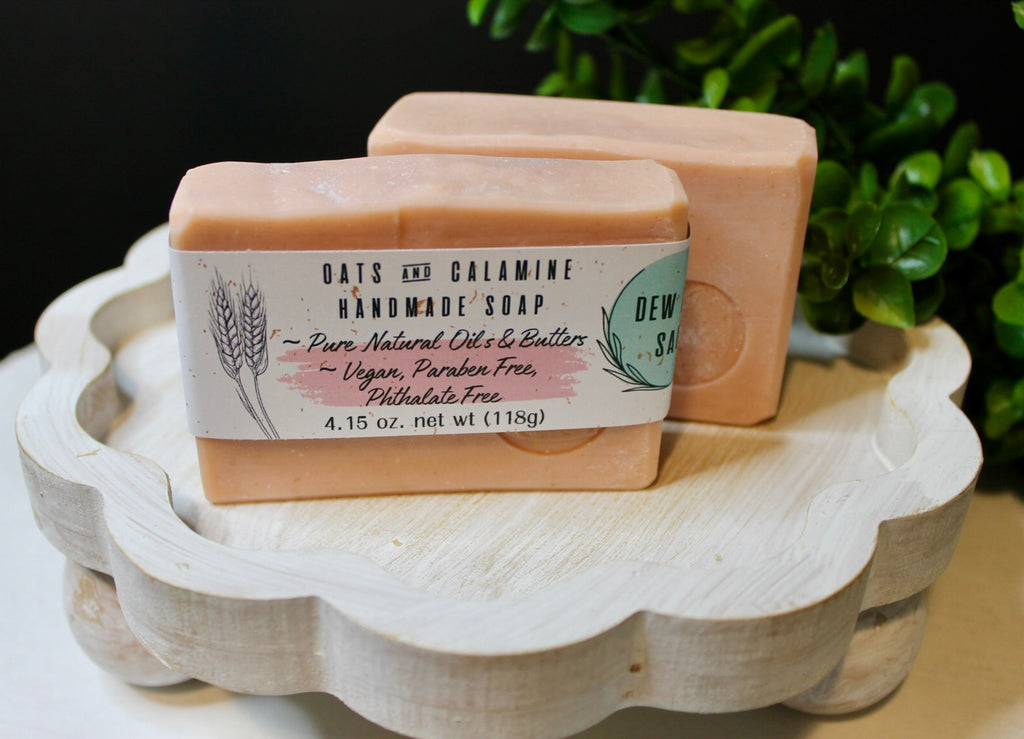 Two bars of soap on a wooden tray with a plant in the background