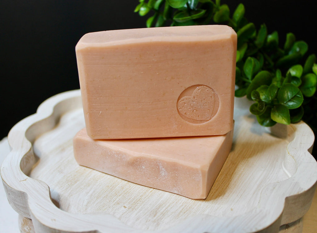 Two bars of soap on a wooden tray with a plant in the background