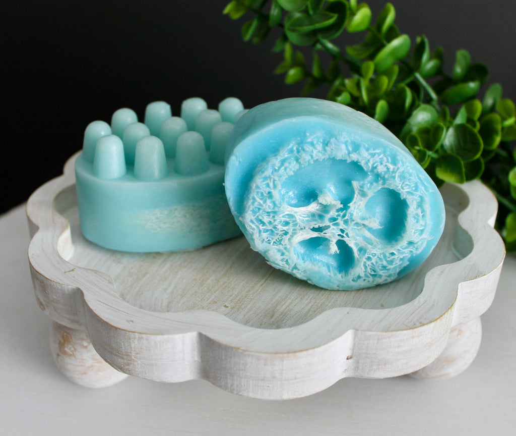 Blue loofah soaps with textured surface on a decorative stand with greenery in the background