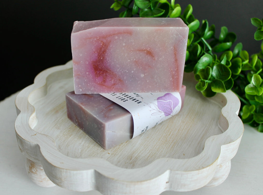 Two purple soap bars on a decorative stand with greenery in the background