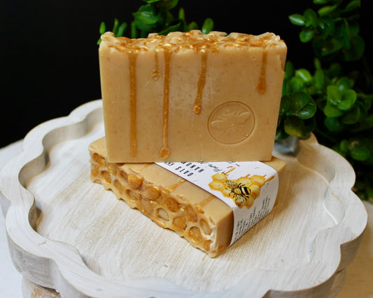 Two bars of honey-scented soap on a decorative white plate with a blurred green plant background.