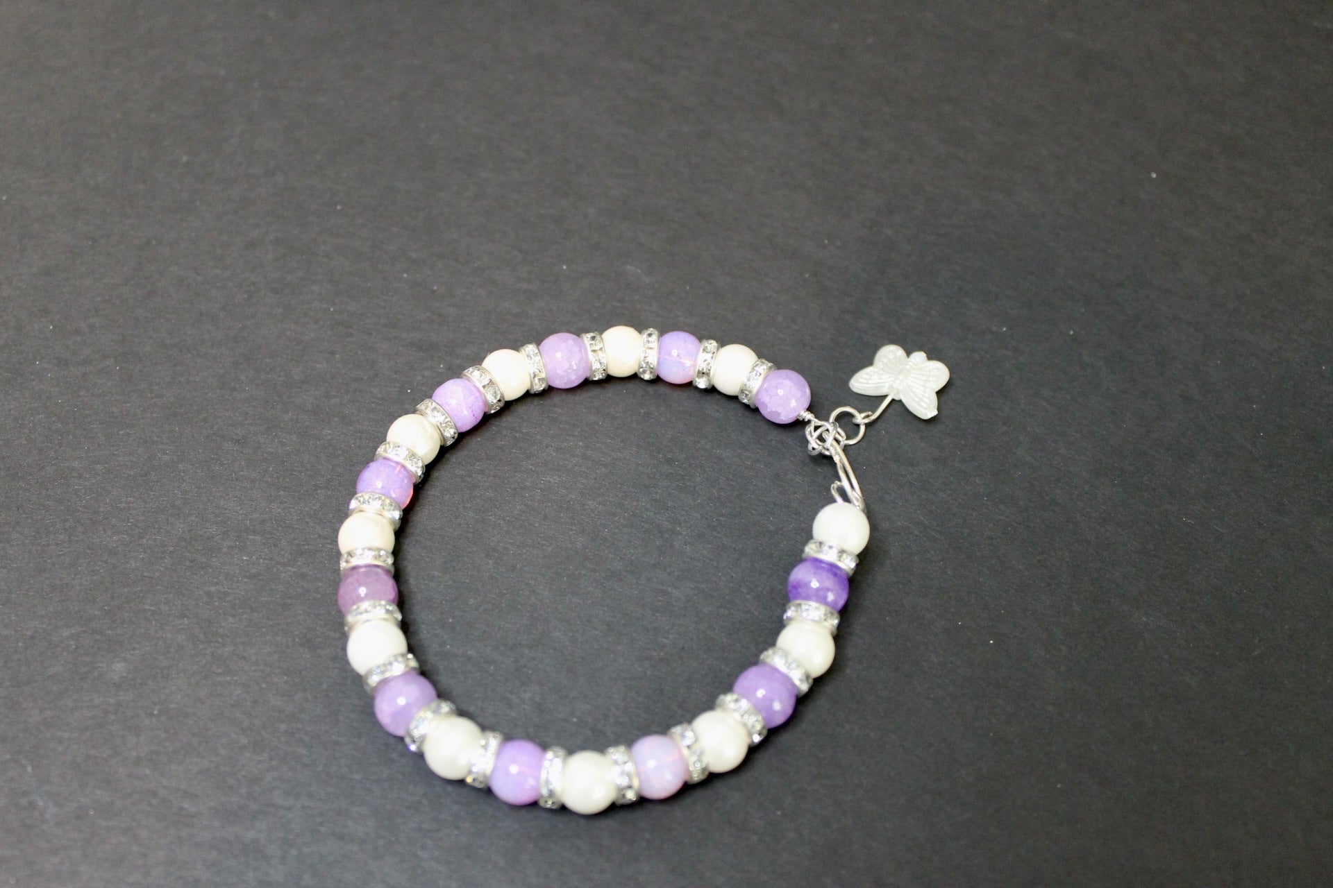 Beaded bracelet with purple and white beads on a dark gray background