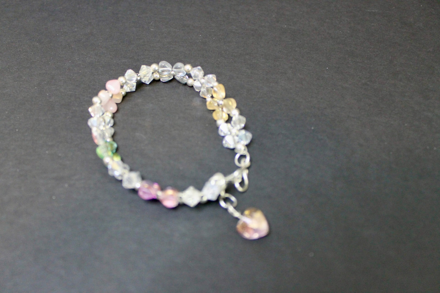 Multicolored beaded bracelet with a heart charm on a dark gray background