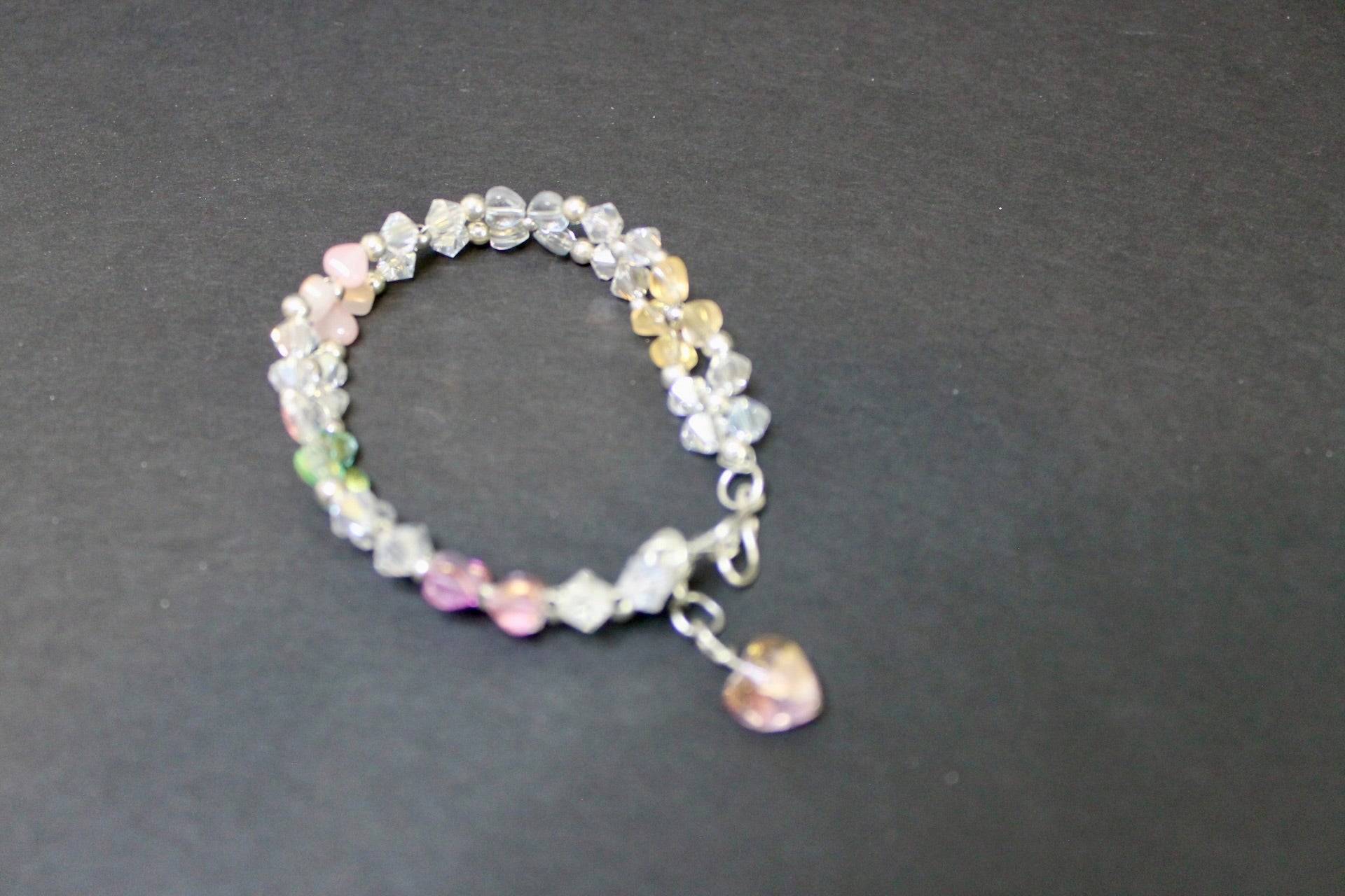 Multicolored beaded bracelet with a heart charm on a dark gray background