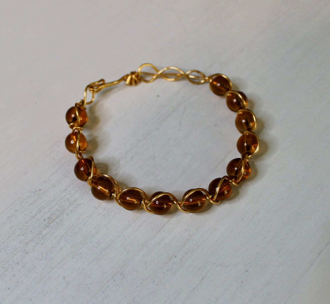 Gold bracelet with brown beads on a light gray background