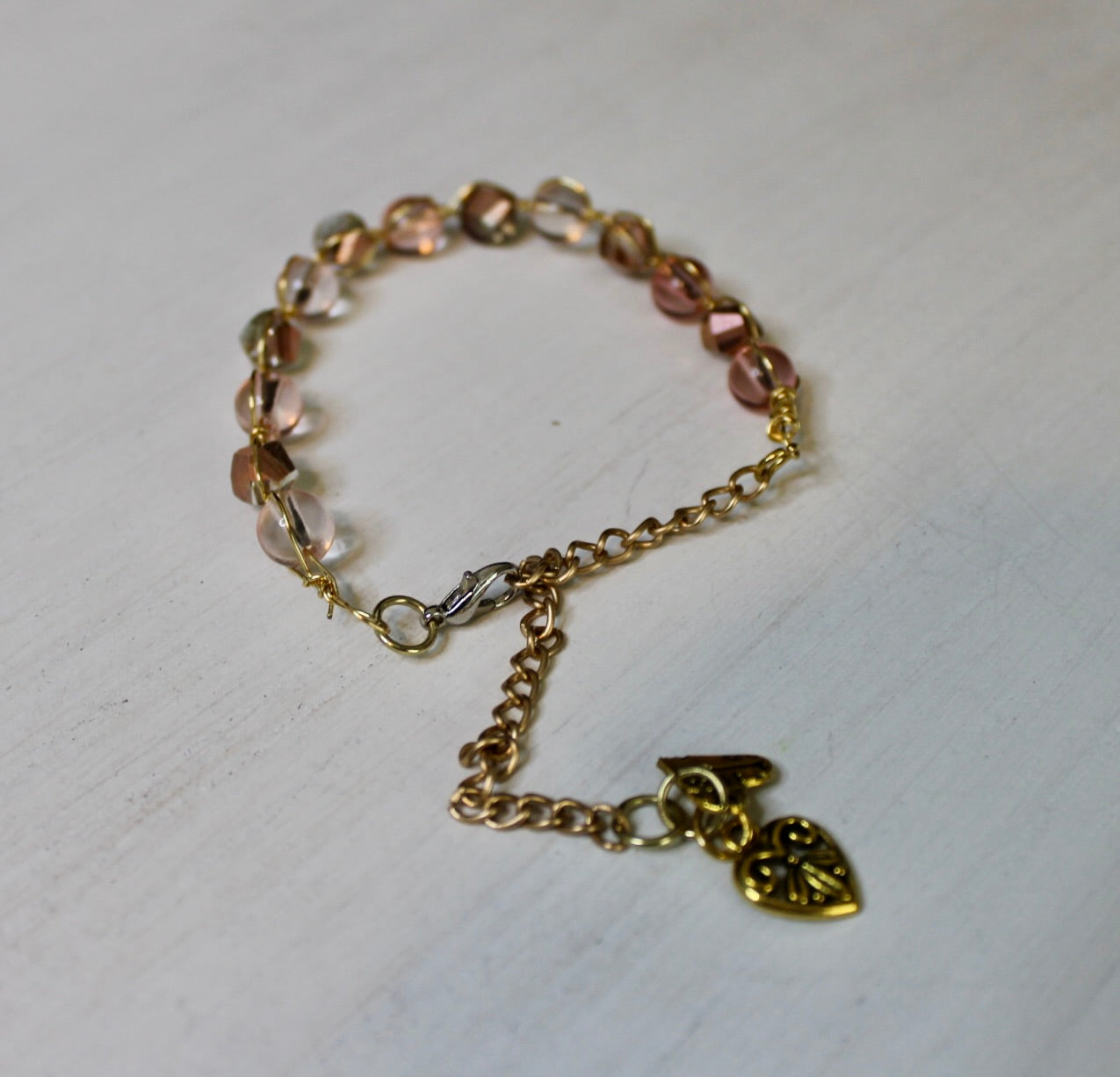 Gold bracelet with heart charm on a light wooden surface
