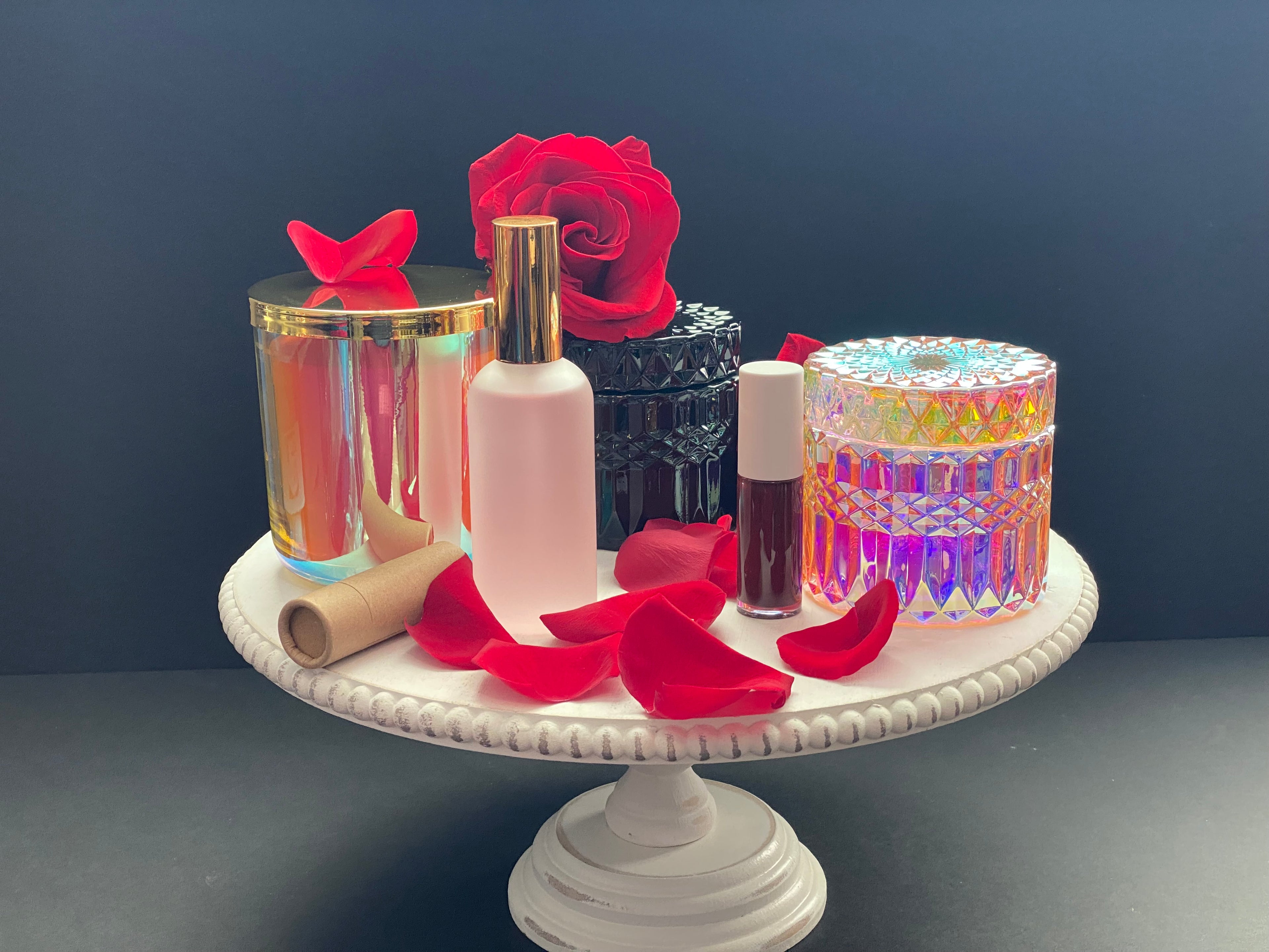 Makeup products and red roses on a white cake stand against a dark background