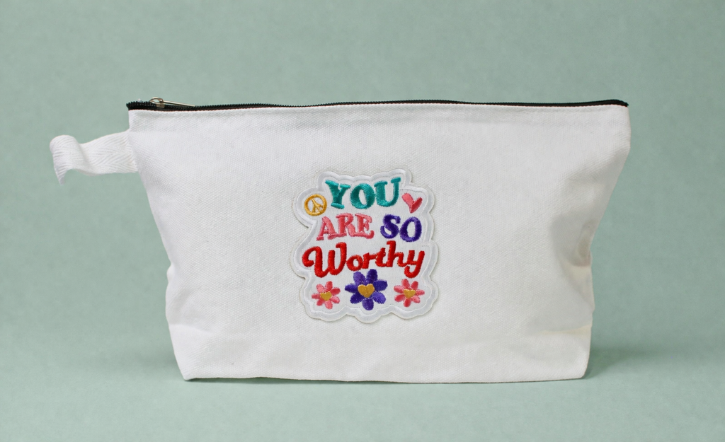 White pouch with motivational quote and flowers on a light gray background