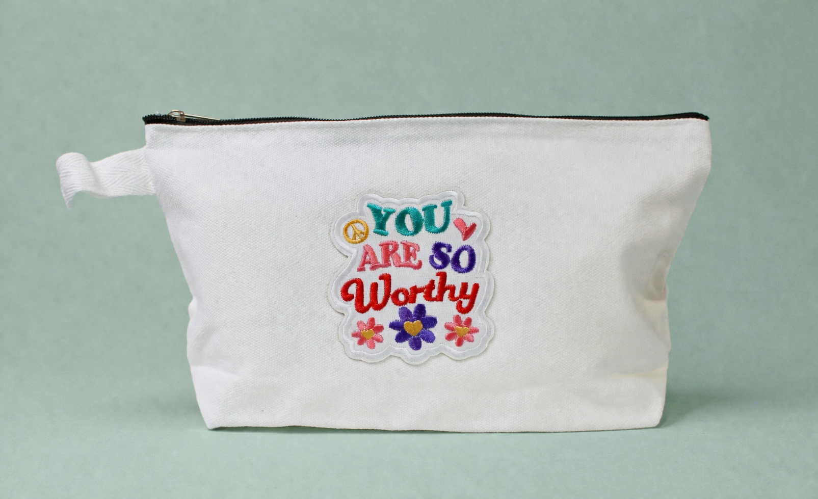 White pouch with motivational quote and flowers on a light gray background